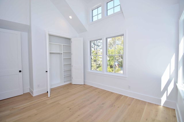 unfurnished bedroom with light wood-style flooring, baseboards, and high vaulted ceiling