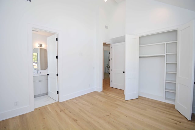 unfurnished bedroom featuring baseboards, a high ceiling, light wood-style flooring, a closet, and ensuite bathroom