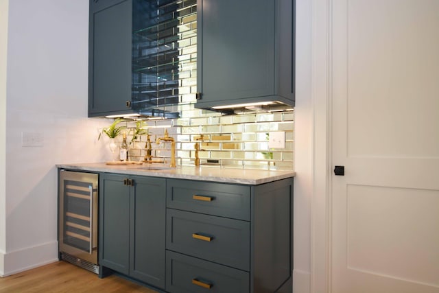 bar featuring light wood finished floors, tasteful backsplash, wine cooler, a dry bar, and a sink