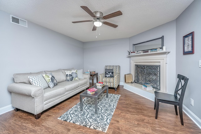 living room featuring ceiling fan, dark wood-type flooring, and a textured ceiling