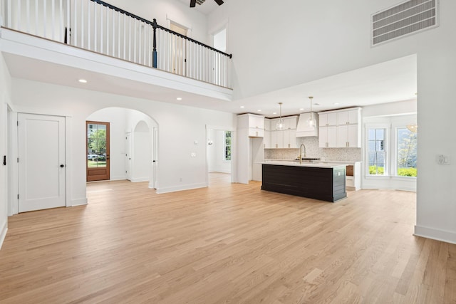 380 Tidal Reef Cir, Mount Pleasant, SC 29464 - unfurnished living room with a towering ceiling, a sink, arched walkways, light wood-style flooring, and healthy amount of natural light