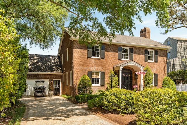colonial-style house featuring roof with shingles, a chimney, brick siding, concrete driveway, and an attached garage