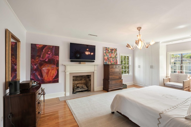 bedroom featuring crown molding, an inviting chandelier, light wood-style flooring, baseboards, and visible vents