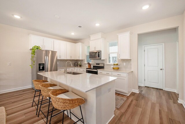 kitchen featuring a kitchen bar, a sink, light wood finished floors, white cabinets, and appliances with stainless steel finishes