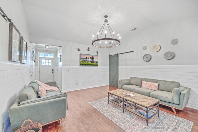 living room with hardwood / wood-style flooring, a notable chandelier, a barn door, and lofted ceiling