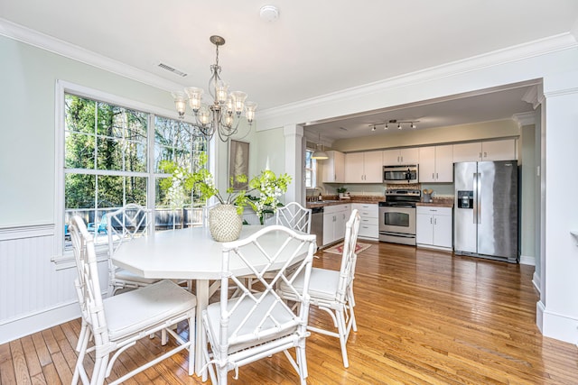 dining area with light wood-style flooring, crown molding, visible vents, decorative columns, and an inviting chandelier