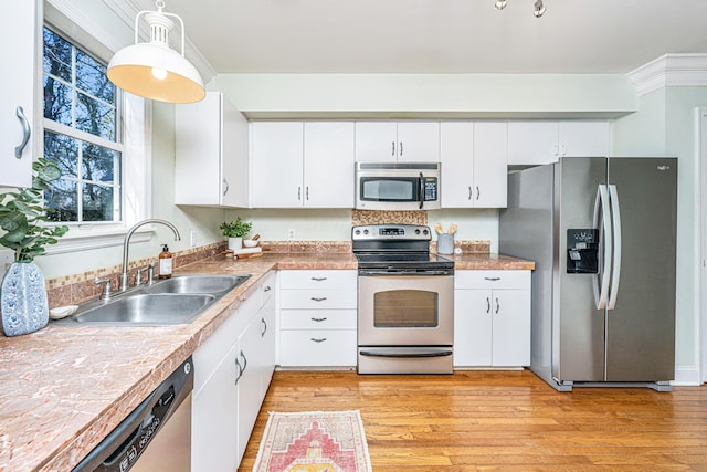 kitchen featuring stainless steel appliances, a sink, white cabinetry, light wood-style floors, and decorative light fixtures