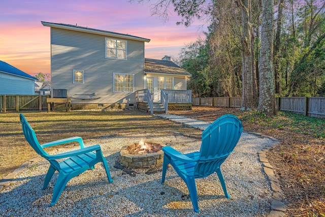 back of property at dusk featuring a yard, an outdoor fire pit, crawl space, a deck, and a fenced backyard