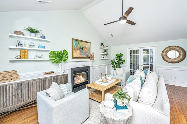 living area featuring light wood finished floors, a glass covered fireplace, radiator, vaulted ceiling, and french doors