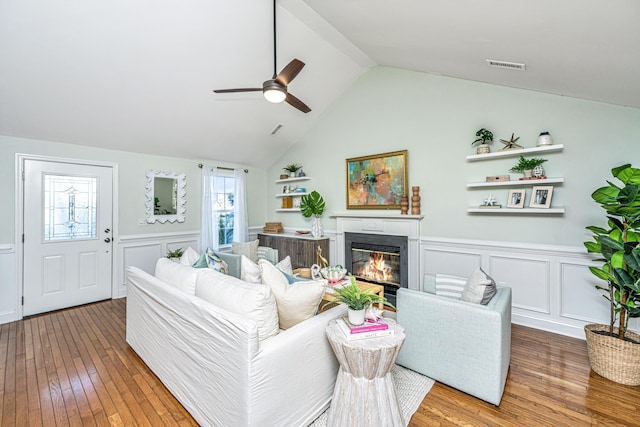 living room featuring lofted ceiling, hardwood / wood-style flooring, visible vents, wainscoting, and a glass covered fireplace