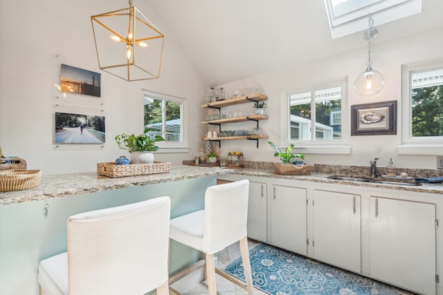 kitchen with vaulted ceiling with skylight, plenty of natural light, pendant lighting, and white cabinets