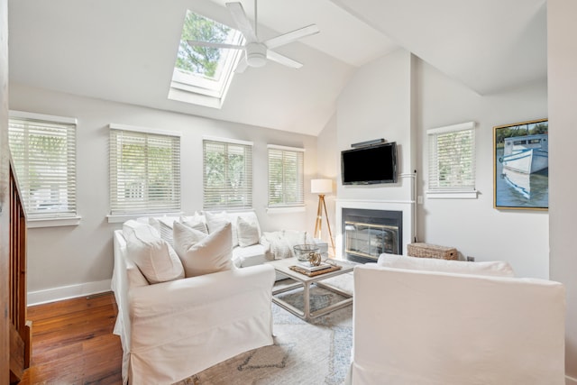 living room with a wealth of natural light, ceiling fan, dark wood-type flooring, and vaulted ceiling with skylight