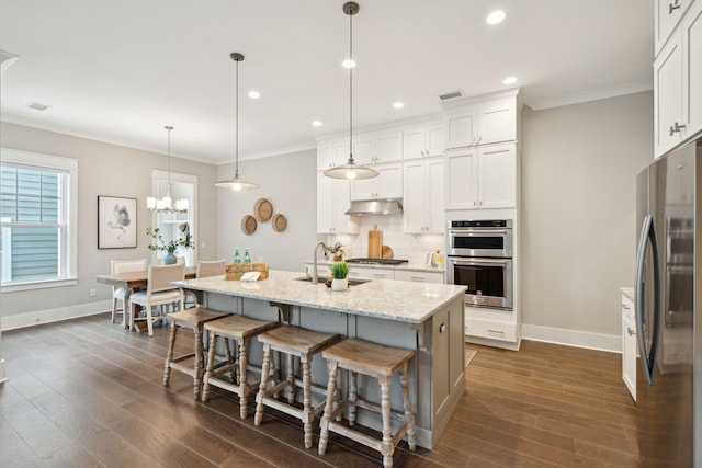 kitchen with a kitchen breakfast bar, stainless steel appliances, white cabinetry, hanging light fixtures, and an island with sink