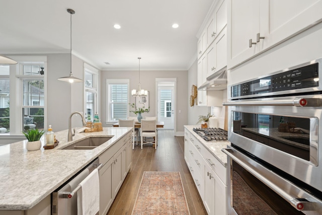 kitchen featuring stainless steel appliances, an island with sink, decorative light fixtures, white cabinets, and ornamental molding