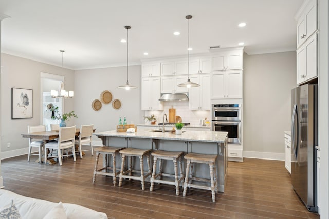 kitchen featuring backsplash, a kitchen island with sink, white cabinets, appliances with stainless steel finishes, and decorative light fixtures