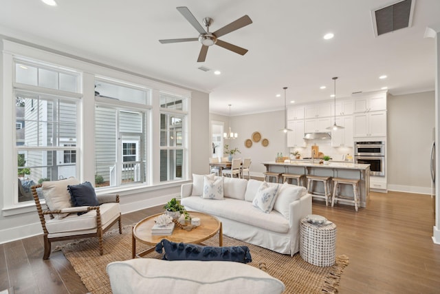 living room featuring ceiling fan with notable chandelier, dark hardwood / wood-style floors, and ornamental molding