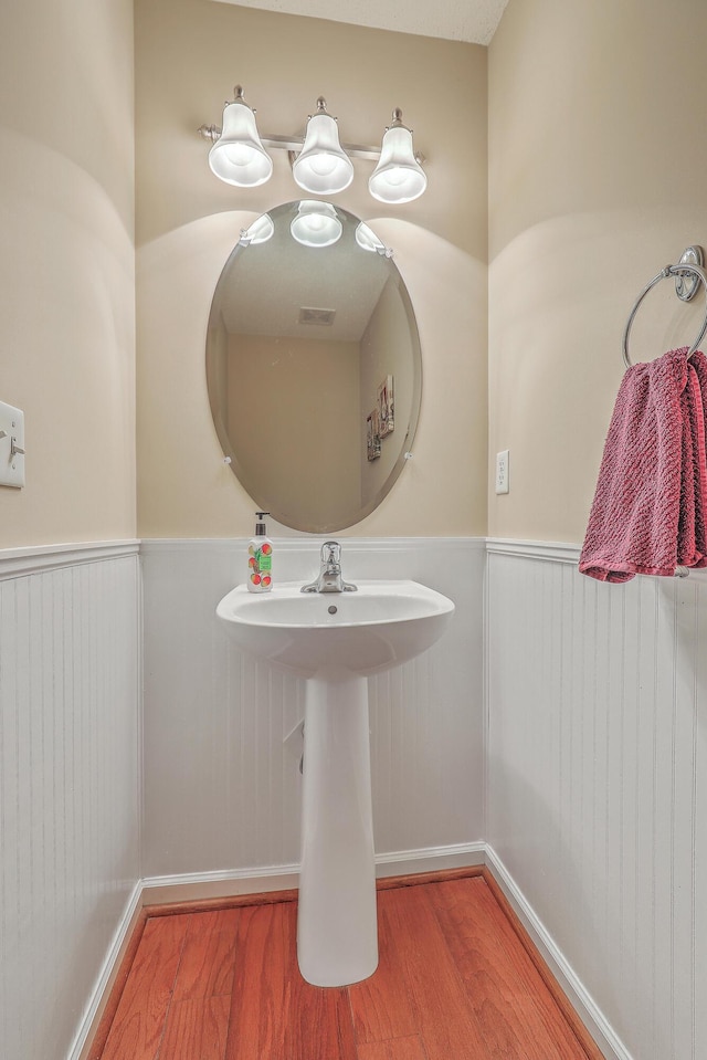 bathroom with a wainscoted wall and wood finished floors