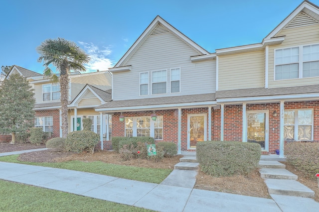 townhome / multi-family property with a shingled roof and brick siding