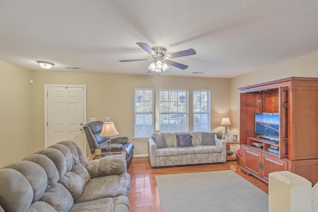 living area with ceiling fan, a textured ceiling, and light wood finished floors