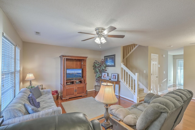 living area with stairs, a textured ceiling, wood finished floors, and visible vents