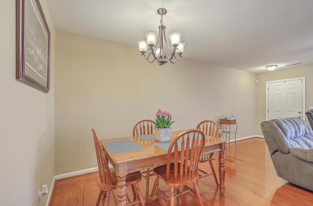 dining area featuring light wood-style floors, a textured ceiling, baseboards, and a notable chandelier