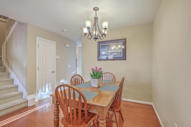 dining area with a textured ceiling, light wood-style flooring, baseboards, stairs, and an inviting chandelier