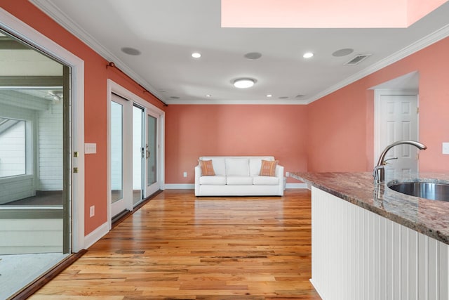 interior space with ornamental molding, sink, light hardwood / wood-style flooring, and dark stone countertops