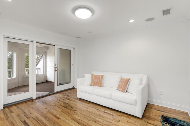 living room featuring light wood-style flooring, baseboards, ornamental molding, and plenty of natural light