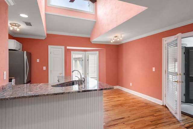 kitchen with stone counters, sink, stainless steel fridge, ornamental molding, and light hardwood / wood-style flooring