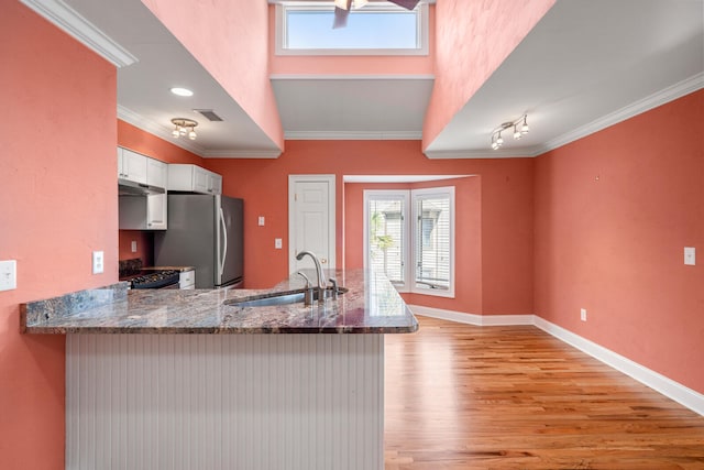 kitchen with white cabinetry, sink, stainless steel fridge, ornamental molding, and kitchen peninsula