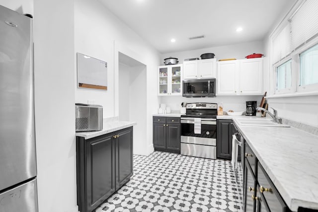 kitchen featuring appliances with stainless steel finishes, a sink, white cabinetry, glass insert cabinets, and light flooring
