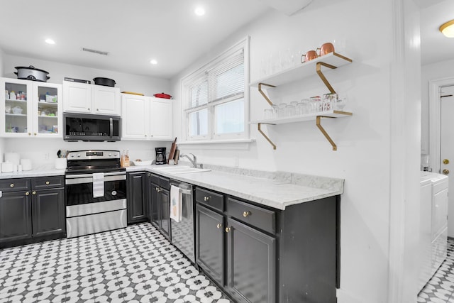 kitchen featuring stainless steel appliances, washer and dryer, a sink, white cabinets, and recessed lighting
