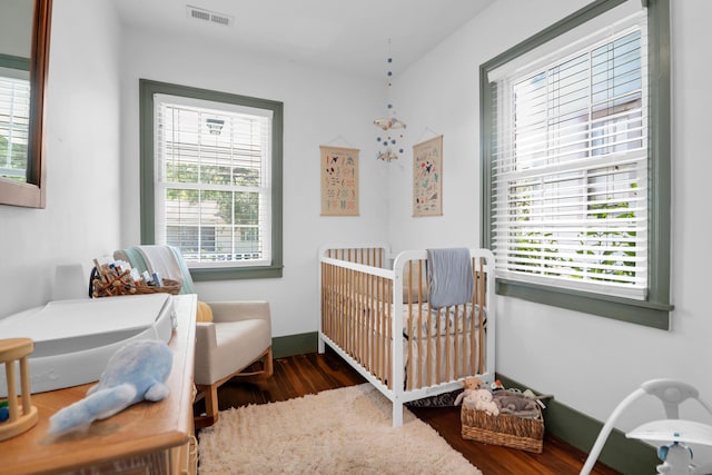 bedroom featuring a nursery area, wood finished floors, and multiple windows
