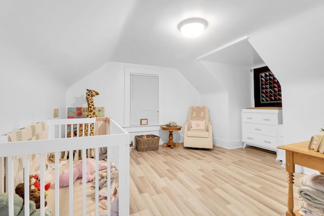 bedroom featuring lofted ceiling, wood finished floors, and a crib