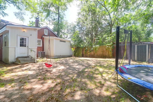 view of yard featuring a trampoline, fence, central air condition unit, an outdoor structure, and a storage shed