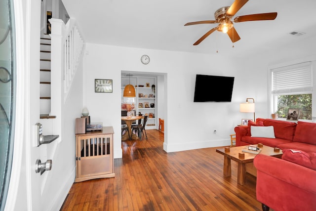 living area with baseboards, ceiling fan, stairs, and dark wood-style flooring