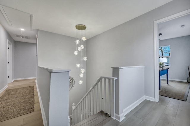 corridor featuring wood finished floors, visible vents, baseboards, an upstairs landing, and attic access