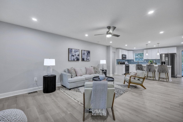 living room with baseboards, visible vents, ceiling fan, and light wood finished floors