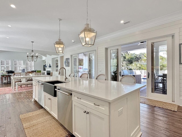 kitchen featuring decorative light fixtures, light countertops, stainless steel dishwasher, open floor plan, and an island with sink