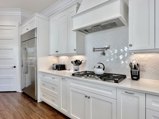 kitchen with white cabinets, custom range hood, appliances with stainless steel finishes, and light countertops