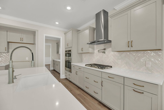 kitchen featuring gray cabinets, wood-type flooring, ornamental molding, stainless steel appliances, and wall chimney range hood