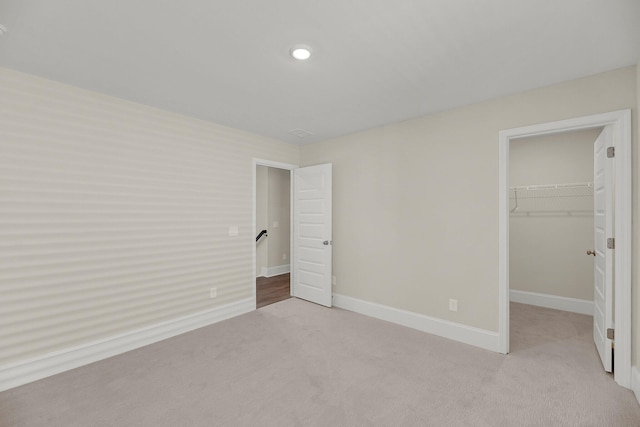 unfurnished bedroom featuring a walk in closet, light colored carpet, and a closet