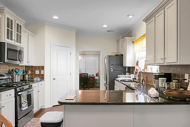 kitchen featuring stainless steel appliances, crown molding, backsplash, sink, and kitchen peninsula