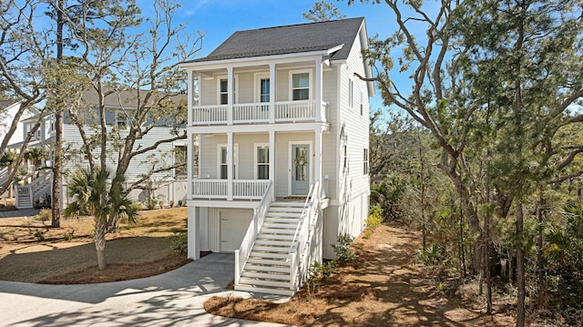 beach home with a balcony, covered porch, a shingled roof, stairs, and concrete driveway