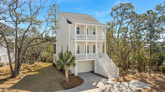 coastal inspired home with a balcony, covered porch, stairs, driveway, and roof with shingles