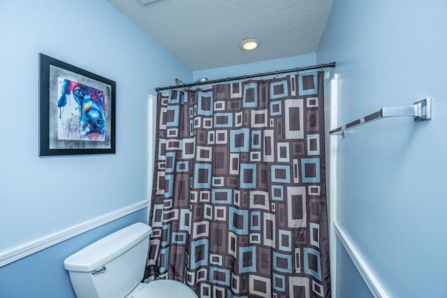 bathroom featuring a shower with shower curtain, toilet, and a textured ceiling