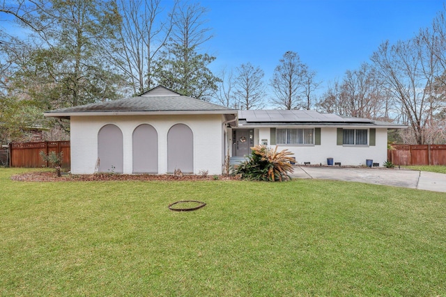 ranch-style home featuring a front lawn, fence, brick siding, and roof mounted solar panels