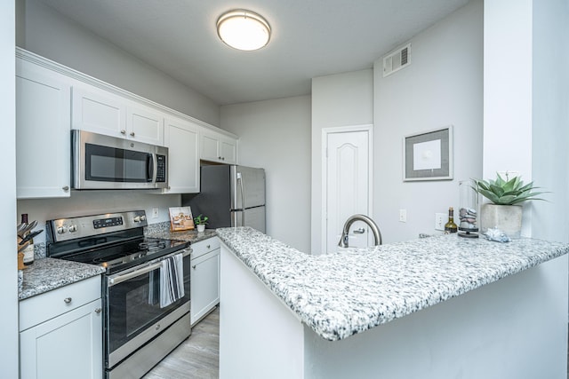 kitchen with light stone countertops, kitchen peninsula, stainless steel appliances, white cabinets, and light hardwood / wood-style flooring