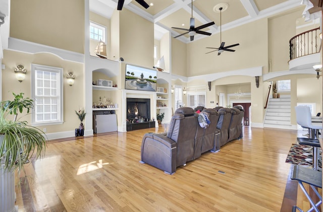 living room with wood finished floors, arched walkways, a lit fireplace, and ceiling fan
