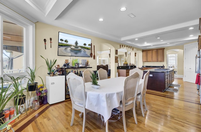dining area with light wood-type flooring, a tray ceiling, arched walkways, and recessed lighting